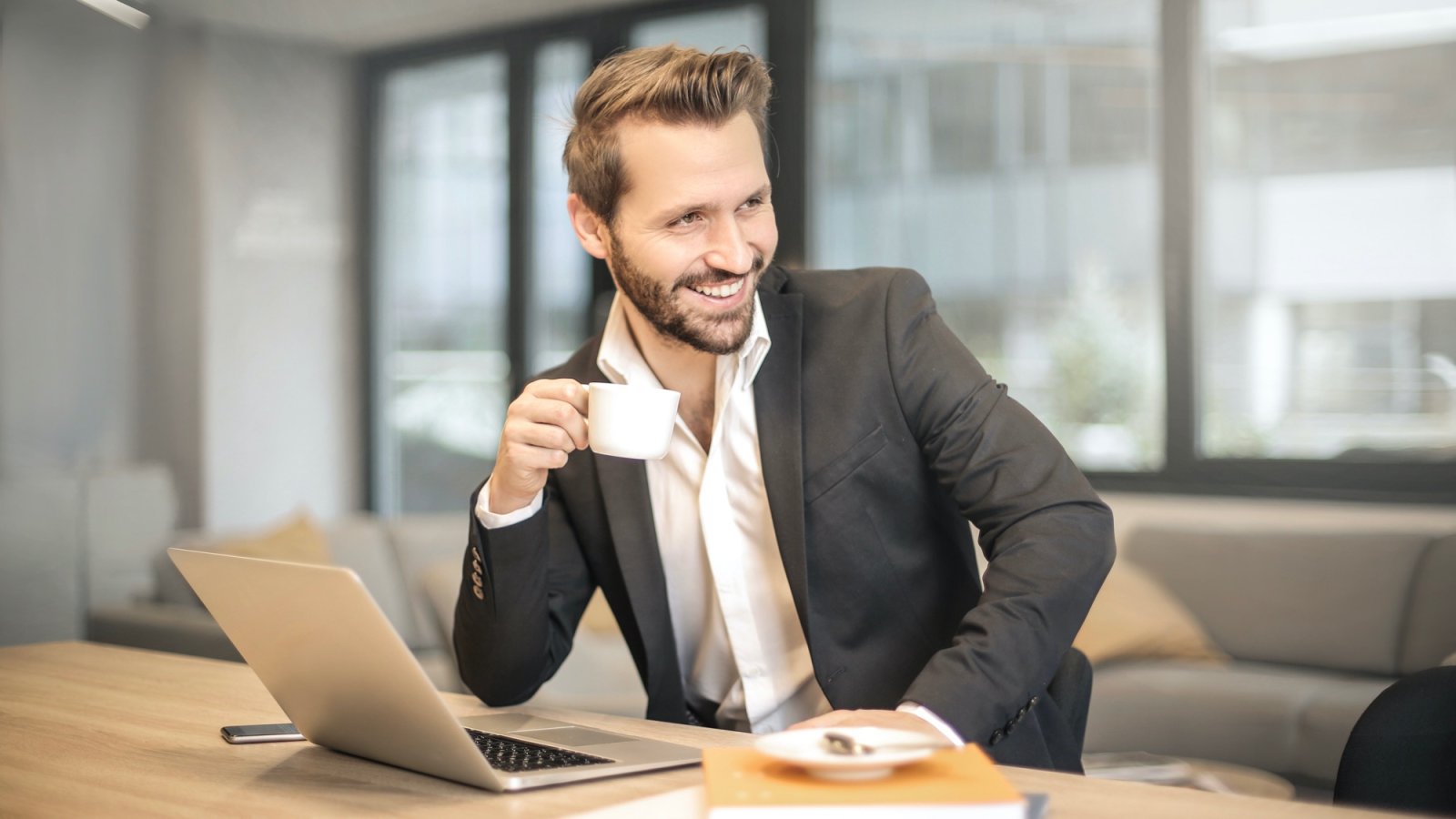 Lächelnder Mann im Sakko mit Kaffeetasse am Laptop – Kundenstimme