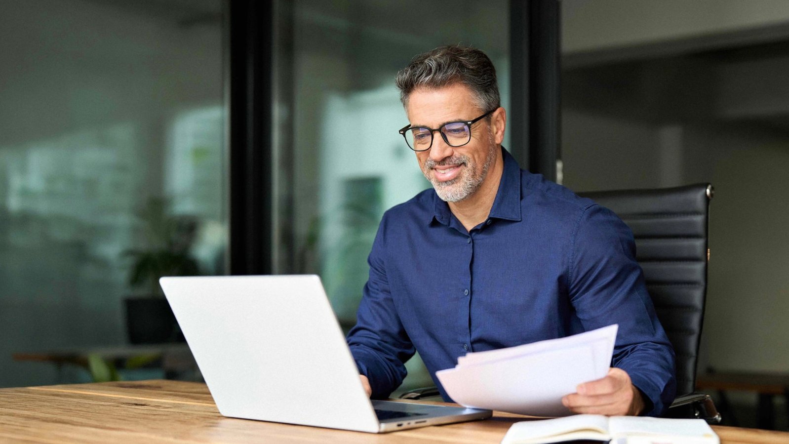 Bewirbdich.ch: Bewerbungshilfe, Job-Coaching, Arbeitszeugnisse und vieles mehr. Mann mit Brille prüft am Schreibtisch Unterlagen und Laptop – Bewerbungshilfe und Coaching
