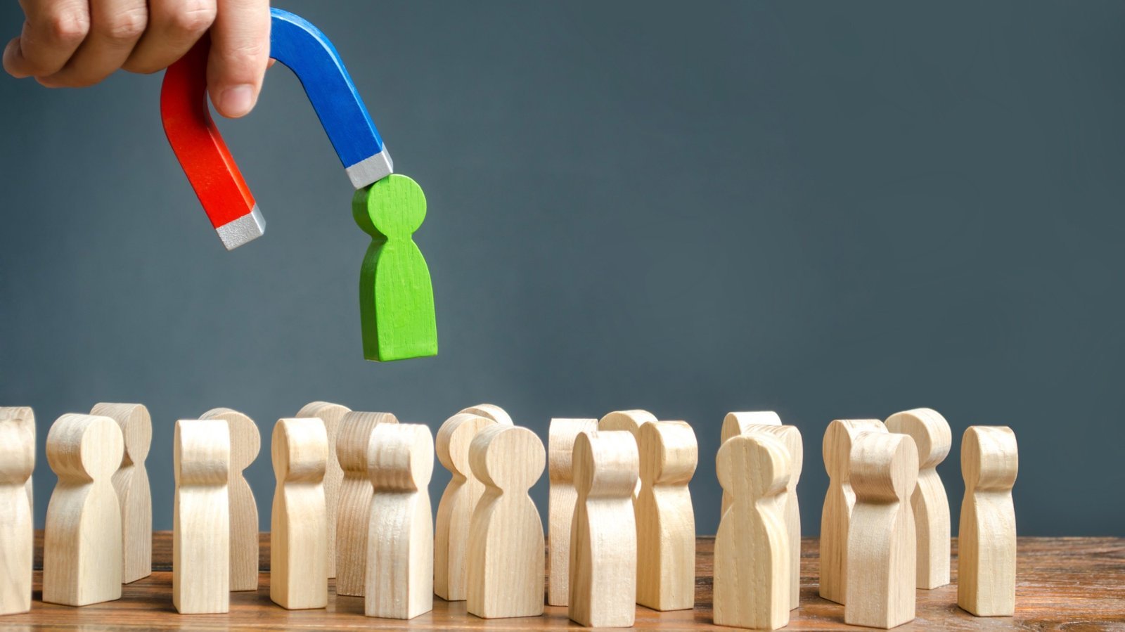 Magnet zieht eine grüne Holzfigur aus einer Reihe heller Figuren – Bewerbungsfehler vermeiden