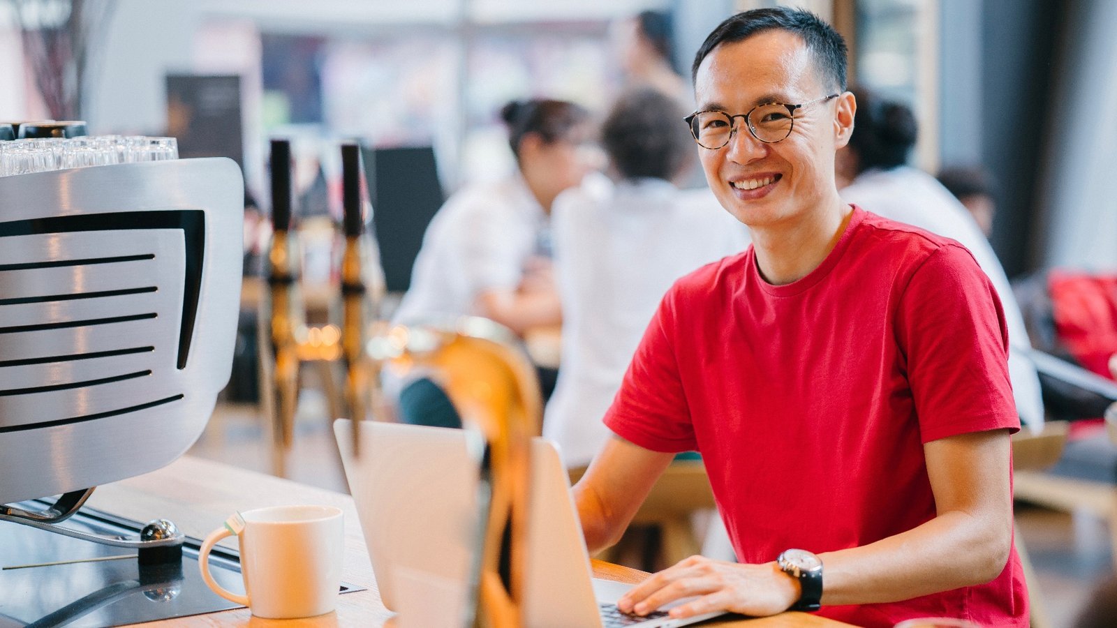 Lächelnder Mann im roten T-Shirt am Laptop in einem Café – beliebte Arbeitgeber