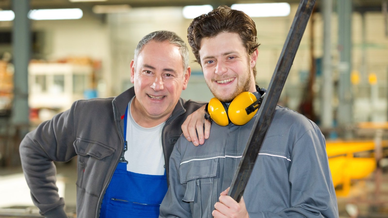 Erfahrener Handwerker legt einem jungen Kollegen den Arm um die Schulter – erster Arbeitstag