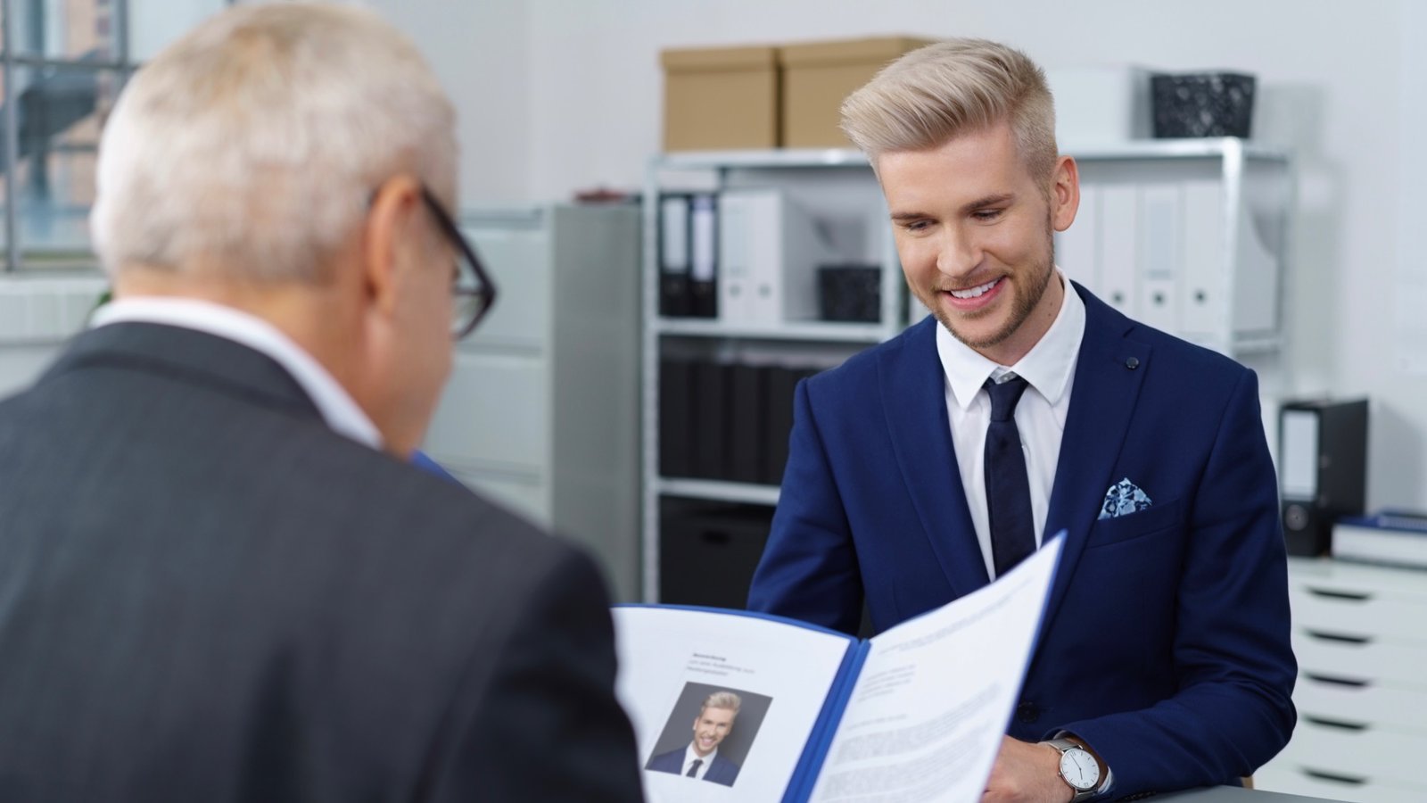 Junger Bewerber überreicht einem Personalverantwortlichen sein Bewerbungsdossier